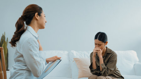 Sad PTSD woman patient in therapy for mental health with psychologist, depression or grief after life failure. Frustrated trauma young woman talking to vivancy psychologist about emotion in clinicの写真素材