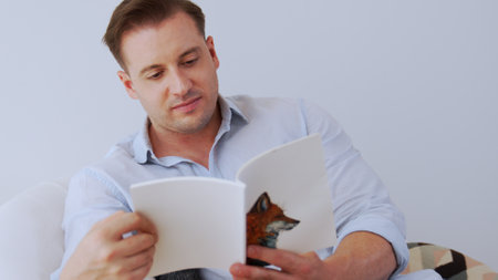 Middle age man sitting on sofa read fable book increase knowledge about social and imagination for occupation or raise children to be good adult as smart father. Lifelong learning concept. Divergence.の写真素材