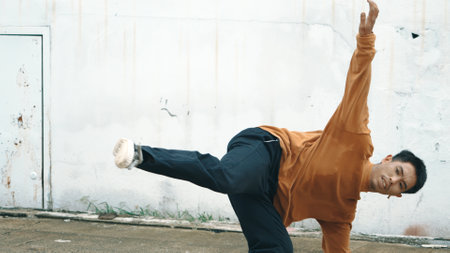Hispanic man stretch arms and dance break dancing in front of wall. Motion shot of stylish street dancer in casual outfit practicing dancing in hip hop style. Outdoor sport 2023. Background. Endeavor.の写真素材