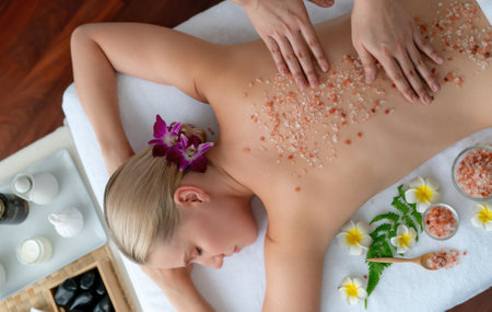 Panorama top view woman customer having exfoliation treatment in luxury spa salon with warmth candle light ambient. Salt scrub beauty treatment in health spa body scrub. Quiescentの写真素材