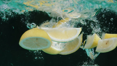 Slices of orange floating in a glass bowl of water with background. Macrography of orange sliced dropping and falling in to clear water with separated dark backdrop. Close up. Slow motion. Pabulum.の写真素材