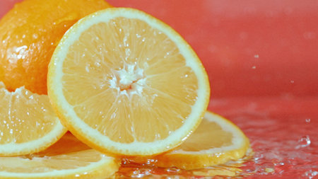 Close up of fresh orange sliced with orange with splashed water at red background. Macrography of slice of citrus fruit with water spilling and water wave at separated wet red backdrop. Pabulum.の写真素材