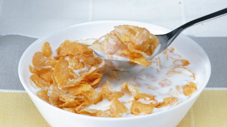 Side view of white bowl with yellow cereal and milk prepare for eating breakfast. Close up of taking...