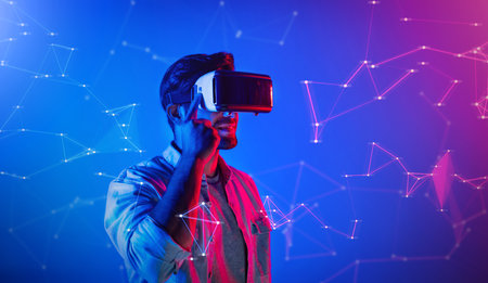 Smart caucasian man wearing VR glasses while standing at neon light. Skilled person using visual...