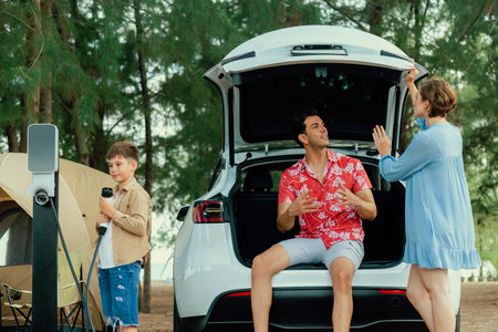 Outdoor adventure and family vacation camping in nature travel by eco friendly car for sustainable future. Lovely family recharge EV car with EV charging station in campsite. Perpetualの写真素材