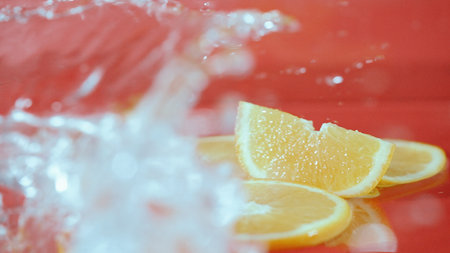 Close up of fresh lemon slices splashing on red background. Macro of sliced lemon dropping and falling in to splashing water. Freshness and hydration concept. Citrus. Design for poster. Pabulum.の写真素材