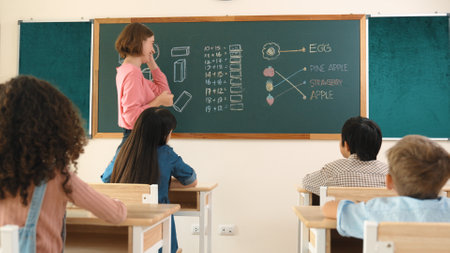 Smart teacher checking cute student homework while explaining idea at class. Attractive instructor walking around classroom while looking at notebook and talking about Math theory to child. Pedagogy.の写真素材