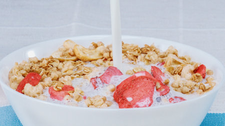 Close up of a white bowl of cereal with milk being poured into it. Macrography of white milk pouring...
