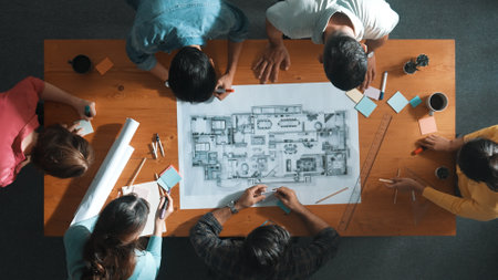 Top down of skilled business people holding tablet an looking at blueprint. Aerial view of architect engineer planning and design house design together while standing at table with laptop. Symposium.の写真素材