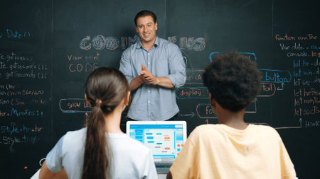 Handsome teacher teaching engineering code to diverse student at blackboard. Happy multicultural highschool children study or learning programing or coding system while using laptop. Edification.の写真素材