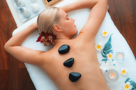 Hot stone massage at spa salon in luxury resort with day light serenity ambient, blissful woman customer enjoying spa basalt stone massage glide over body with soothing warmth. Quiescentの写真素材