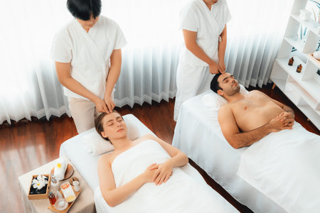 Caucasian couple enjoying relaxing anti-stress head massage and pampering facial beauty skin recreation leisure in dayspa modern light ambient at luxury resort or hotel spa salon. Quiescentの写真素材