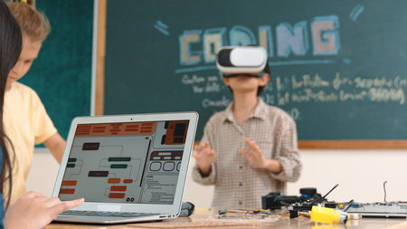 Asian boy wearing VR headset to enter metaworld at table with electronic board while girl coding...