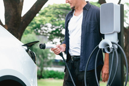 Man recharging battery for electric car during road trip travel EV car in natural forest or national park. Eco friendly travel during vacation and holiday. Exaltの写真素材