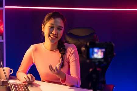 Smiling creative young beautiful Asian influencer recording on camera with positive podcast speech...