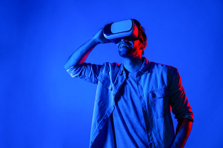 Man with VR goggles and looking at metaverse or simulated virtual world program in neon light background. Caucasian teenager touch virtual reality headset while using technology innovation. Deviation.の写真素材