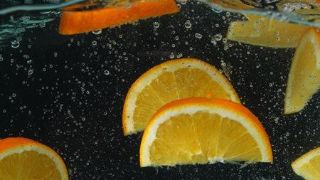 Slices of orange floating in a glass bowl of water with background. Macrography of orange sliced dropping and falling in to clear water with separated dark backdrop. Close up. Slow motion. Pabulum.の写真素材