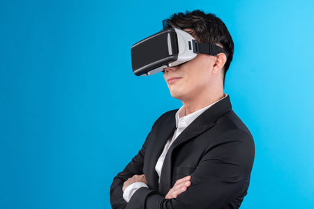 Smiling Asian businessman looking thorough VR connecting to business world report in futuristic metaverse, analyzing innovation technology ads in virtual reality isolated blue copyspace. Contrivance.の写真素材