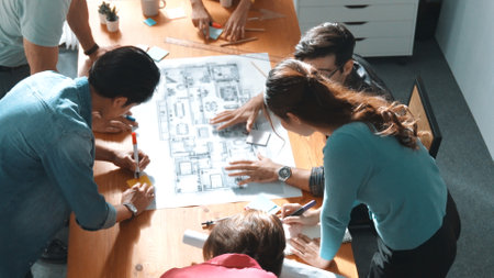 Top view of smart civil engineer working and writing blueprint while sitting at meeting table with...