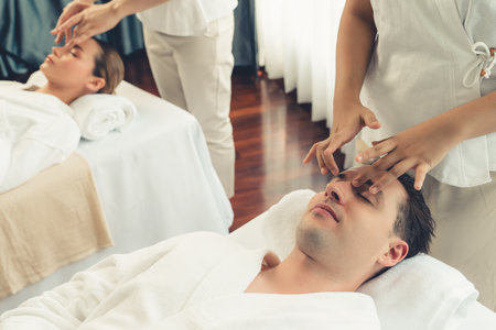 Caucasian couple enjoying relaxing anti-stress head massage and pampering facial beauty skin recreation leisure in dayspa modern light ambient at luxury resort or hotel spa salon. Quiescentの写真素材