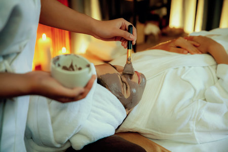 Serene ambiance of spa salon, woman customer indulges in rejuvenating with charcoal face cream massage with warm lighting candle. Facial skin treatment and beauty care concept. Quiescentの写真素材