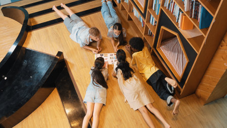 Group of diverse children lying down in circle while reading a book at library. Top view of girl sharing a magazine while pointing at interested topic and talking with lovely friends. Edification.の写真素材