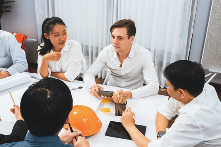 Diverse group of civil engineer and client working together on architectural project, reviewing construction plan and building blueprint at meeting table. Prudentの写真素材