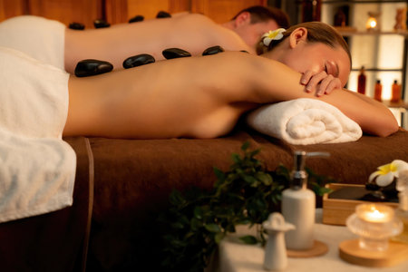 Hot stone massage at spa salon in luxury resort with warm candle light, blissful couple customer enjoying spa basalt stone massage glide over body with soothing warmth. Quiescentの写真素材