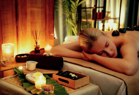Hot stone massage at spa salon in luxury resort with warm candle light, blissful woman customer enjoying spa basalt stone massage glide over body with soothing warmth. Quiescentの写真素材