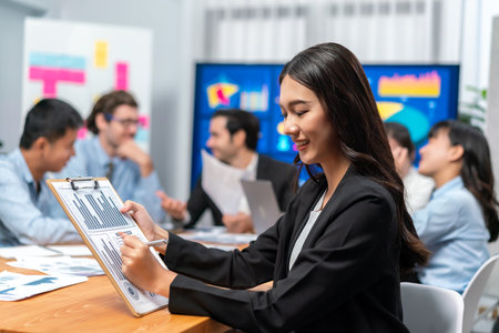 Portrait of happy young asian businesswoman or analyst looking at camera with her colleague analyzing data analysis in dynamic business strategy investment planning meeting. Habilimentの写真素材