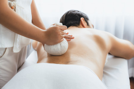 Hot herbal ball spa massage body treatment, masseur gently compresses herb bag on man body. Tranquil and serenity of aromatherapy recreation in day lighting ambient at spa salon. Quiescentの写真素材