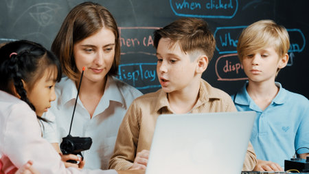 Caucasian boy using laptop programing engineering code and writing program while young caucasian teacher holding controller in STEM technology classroom at blackboard written with prompt. Erudition.の写真素材