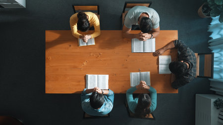 Top down aerial view of smart team hold hands on the holy bible and praying god while sitting at meeting table. Group of people hand folded in prayer with faith, spirituality and religion. Symposium.の写真素材