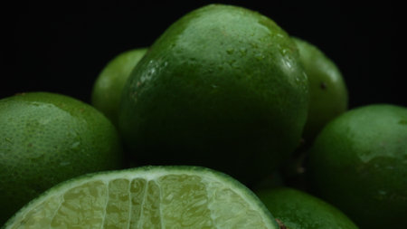 Slices of lime are meticulously arranged in a pile, set against a black background. Each lime slice is captured in stunning detail, its vibrant green hue and enticing texture. Close up. Comestible.の写真素材