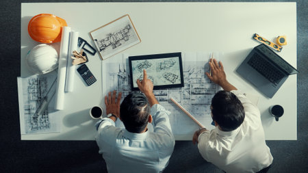 Top view of skilled civil engineer working together to plan building design. Top down aerial view of skilled architect team sitting at table while manager using tablet open project plan. Alimentation.の写真素材