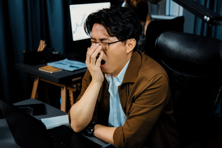 Working businessman feeling extremely sleepy with yawning while working on desk with unfinished...