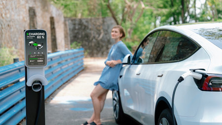 Holiday road trip vacation by the green countryside nature with beautiful young woman recharging electric vehicle with alternative energy. Environmental friendly travel wit EV car. Perpetualの写真素材