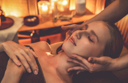 Caucasian woman enjoying relaxing anti-stress head massage and pampering facial beauty skin recreation leisure in warm candle lighting ambient salon spa in luxury resort or hotel. Quiescentの写真素材