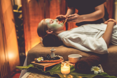 Serene ambiance of spa salon, woman customer indulges in rejuvenating with luxurious face cream massage with warm lighting candle. Facial skin treatment and beauty care concept. Quiescentの写真素材