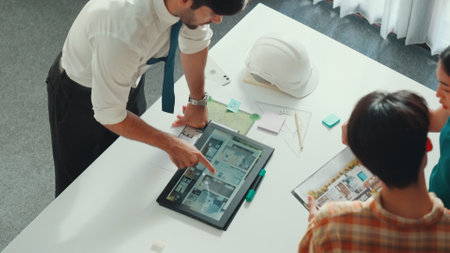Top down view of manager pointing at house model and explain building design. Aerial view of architect engineer brainstorming about interior construction while tablet display house plan. Alimentation.の写真素材