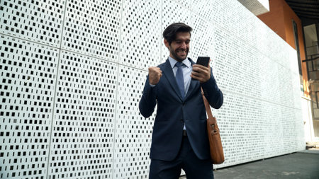 Happy smart business man celebrate for getting promotion or receive good news while walking at street. Skilled project manager or leader express feeling of overjoy at architectural building. Exultantの写真素材