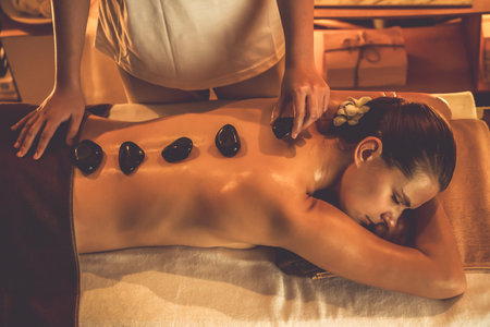 Hot stone massage at spa salon in luxury resort with warm candle light, blissful woman customer enjoying spa basalt stone massage glide over body with soothing warmth. Quiescentの写真素材