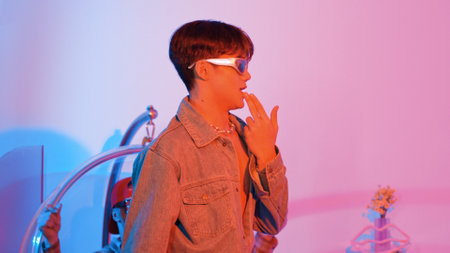 Close up of asian street dancer moving to pop music with neon light while diverse friend sitting and support performance. Professional performer practicing dancing step to beat at studio. Regalement.の写真素材