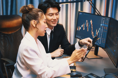 Businessman holding tablet on dynamic stock exchange statistic online showing to partners to share, comparing with high or low point graph on computer screen at night neon modern office. Infobahn.の写真素材