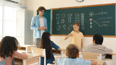 Smart boy pointing at diverse friend while attractive children sitting at class. Elementary student talking and explain idea to caucasian teacher listening while standing in front of class. Pedagogy.の写真素材