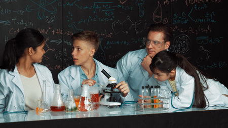Multicultural student looking under microscope while cute girl inspect sample. Teacher looking after...