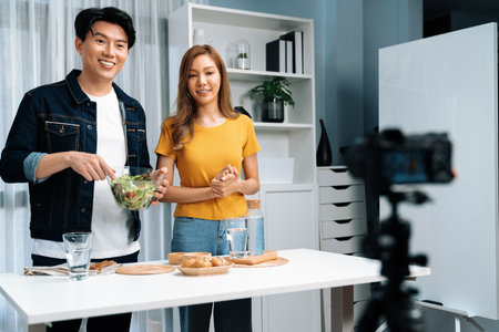 Cooking show live streaming with two chef influencers making mixed salad, all ingredients with dressing with good taste for easy special menu served with bun bread on table record by camera. Infobahn.の写真素材