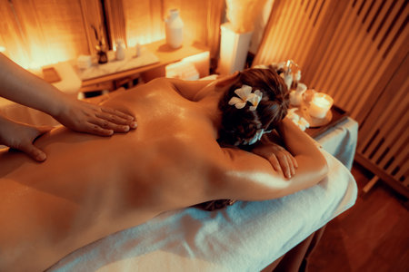 Closeup woman customer enjoying relaxing anti-stress spa massage and pampering with beauty skin recreation leisure in warm candle lighting ambient salon spa at luxury resort or hotel. Quiescentの写真素材