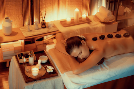 Hot stone massage at spa salon in luxury resort with warm candle light, blissful woman customer enjoying spa basalt stone massage glide over body with soothing warmth. Quiescentの写真素材