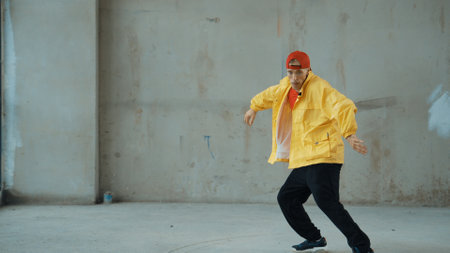 Caucasian hipster shows or practicing footstep at street, urban city. Motion shot of young stylish break dancer moving and stretch arm and leg. Outdoor sport 2024. Gray background. Hiphop.の写真素材